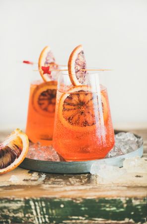 Two glasses of an orange cocktail with blood orange slices, and cocktail picks, vertical composition