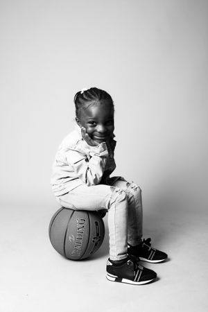 Grayscale photo of girl sitting on basketball against light background