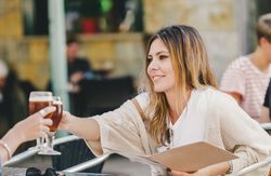 woman clinking glass with friend in outside cafe