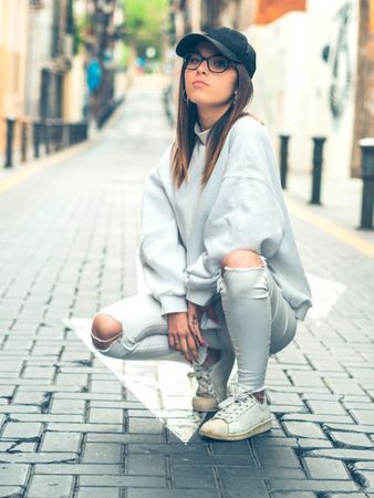Young trendy woman sitting against street