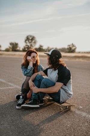 Skaters sitting on empty rural road chatting in sunlight