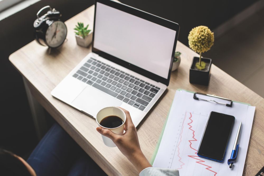 Person holding a cup of coffee while sitting at a desk with laptop in office