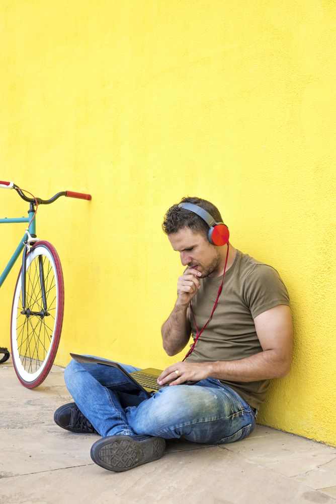 Focused male with red headphones sitting outside looking at laptop