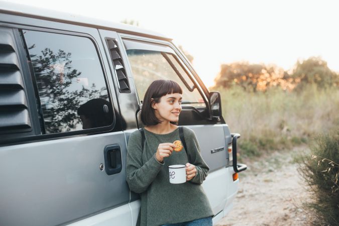 Woman leaning on camper van with snacks and coffee