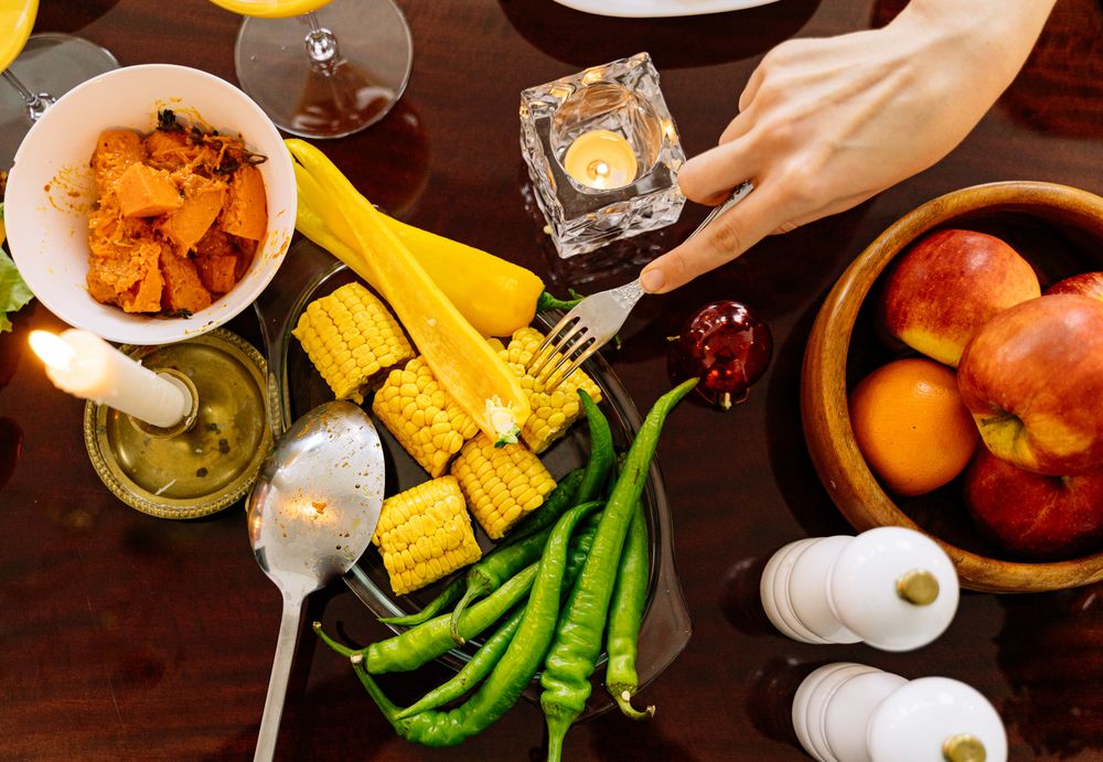 Top view of hand holding a fork beside dish of corn and green chili on plate