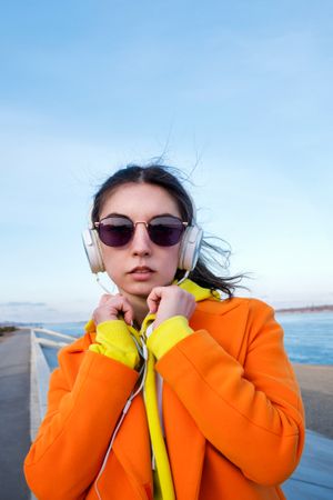 Woman in colorful clothes and sunglasses wearing headphones on the coast