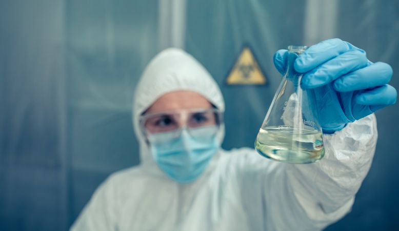 Scientist with protection suit looking test tube in the laboratory