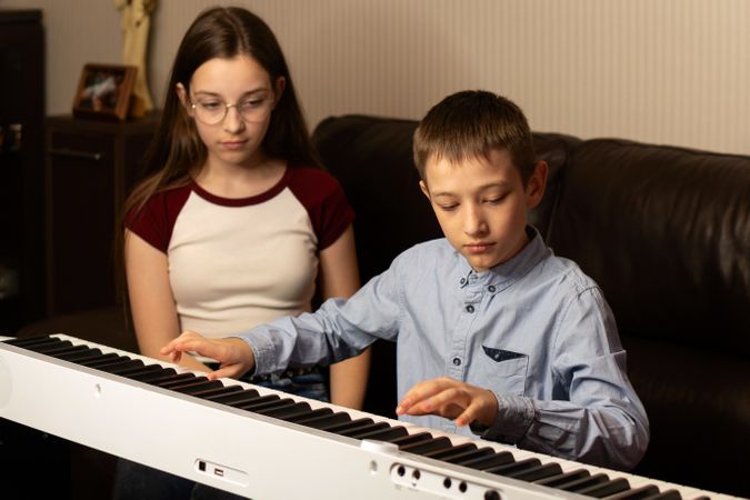 Girl watching as boy plays the keyboard with concentration.