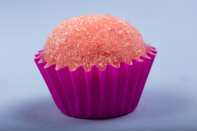 Close up of a single pink strawberry truffle with sugar on blue table