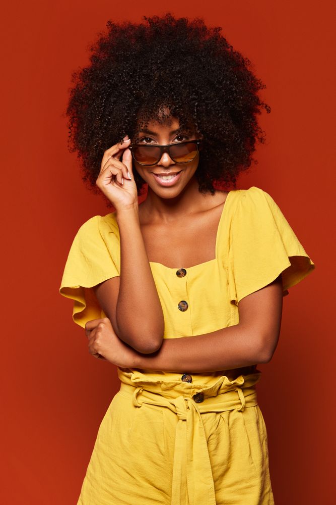 Bright Black woman with hands behind head smiling at camera