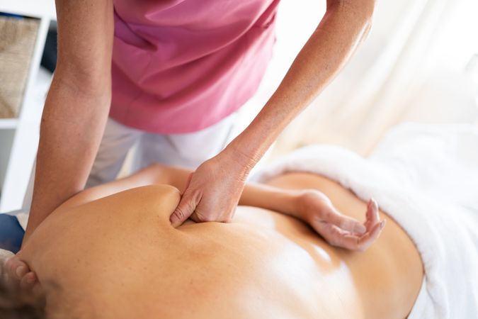 Masseuse kneading back of woman in spa salon using fists