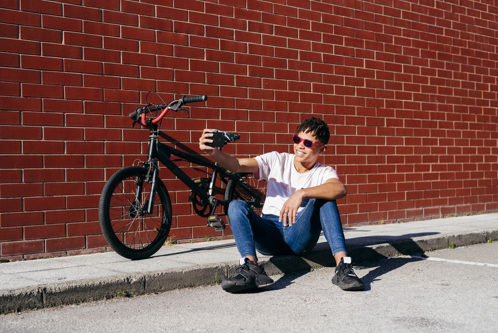 Young happy Black male taking selfie with smartphone near bike