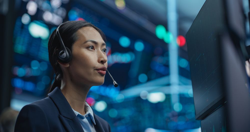 Asian Female Stock Exchange Broker Working on Computer with Stock Information, Commodities and Exchange Market Charts