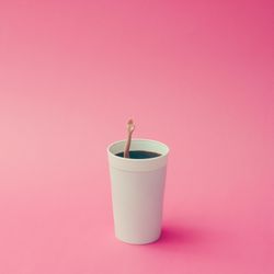 Coffee cup with female doll hand on pink background, with copy space