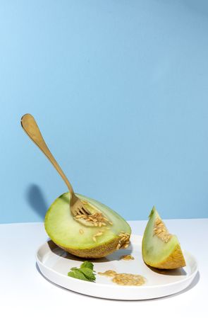 Sliced small melon on plate with spoon and fork