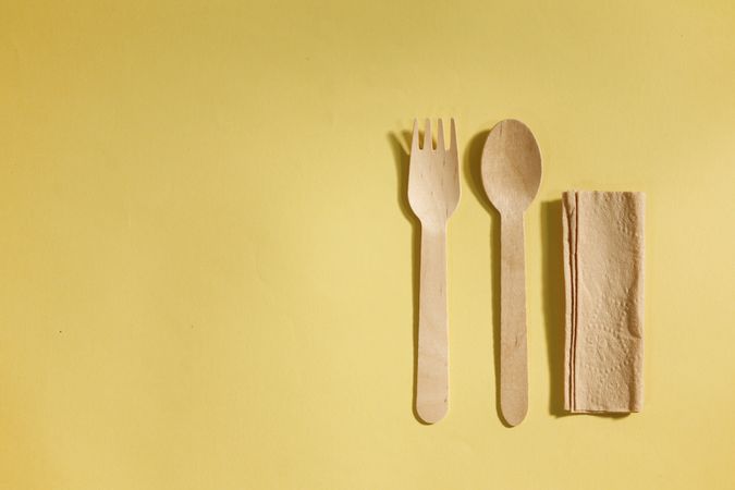 Disposable fork, spoon and napkin on yellow background with copy space