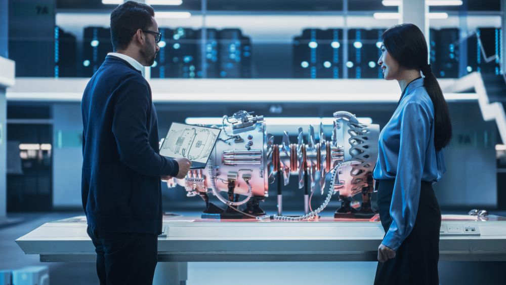 Two Multiethnic Employees Standing in a Modern High Tech Research Facility with Futuristic Turbine Motor.