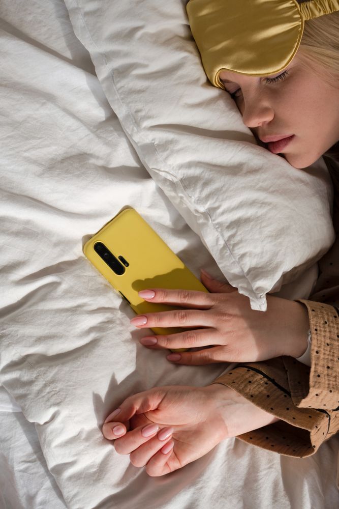 Woman asleep with phone, wearing eye mask