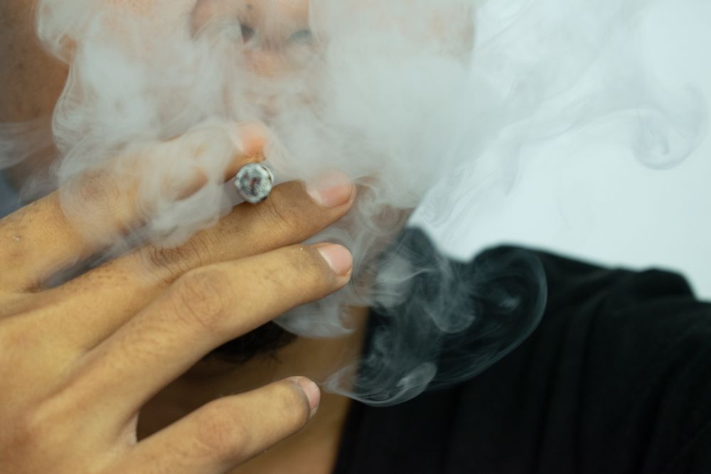 Smoking obscuring man holding a lit cigarette to their mouth