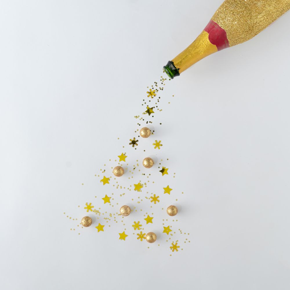 Gold champagne bottle pouring glitter into the shape of a Christmas tree