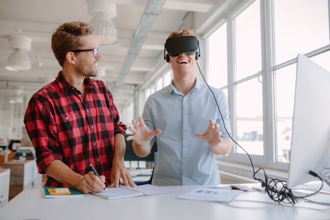 Shot of two young men testing virtual reality glasses in office