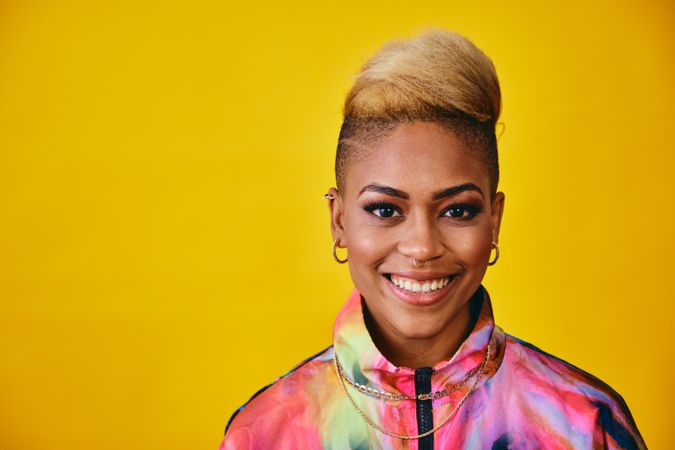 Studio shot of joyful Black woman in bold 80s windbreaker jacket and gold jewelry