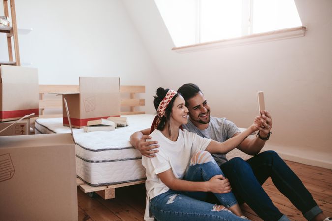 Excited boyfriend and girlfriend taking selfie in new apartment