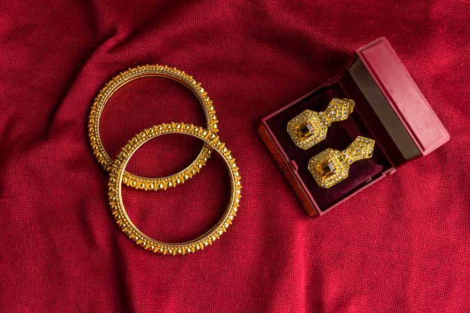 Beautiful shiny golden bangles and diamond studded traditional earrings on a red velvet background