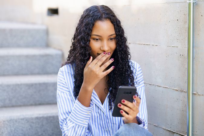 A Young Woman is Intently Engaged with Her Smartphone while Sitting on the Steps