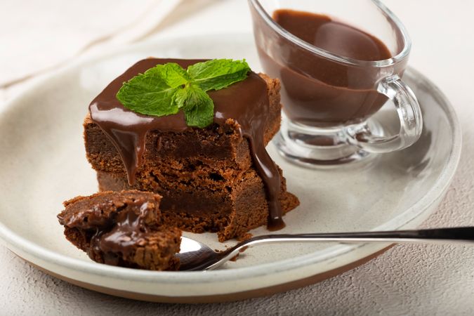 Brownies on plate with spoon served with pot of chocolate sauce and mint garnish