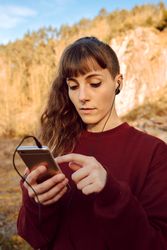 Young woman with piercing listening music on smartphone on hill