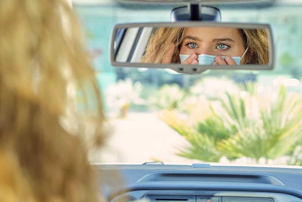 Crop woman putting on face mask against auto mirror