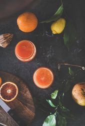 Two glasses of freshly squeezed blood orange juice, with squeezer, and fruit, top view