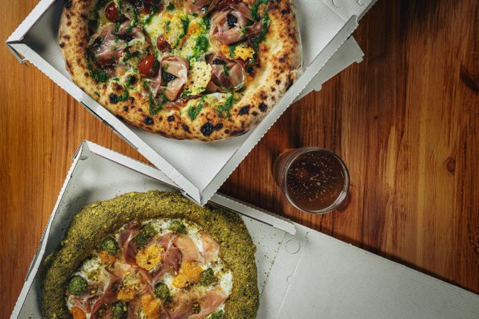 Person cutting Italian pizza with basil, cheese, and ham on rustic plate