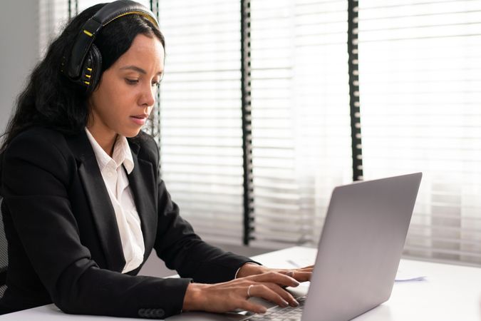Woman wearing headphones while concentrating on typing on laptop