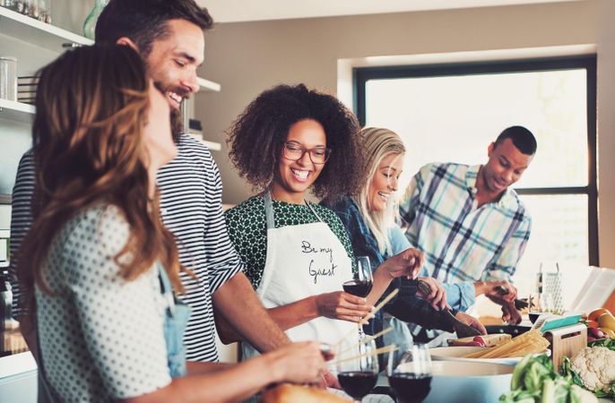 Multi-ethnic friends drinking and cooking pasta in a large kitchen