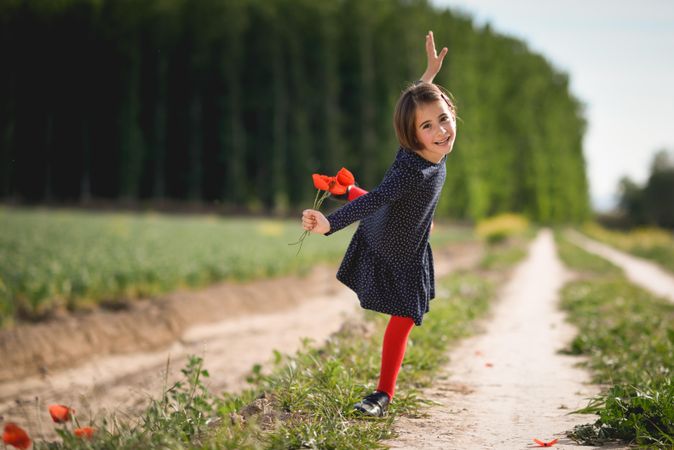 Happy girl on one leg with red flowers in her hand