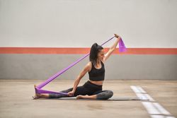 Adult sportswoman stretching body with resistance band