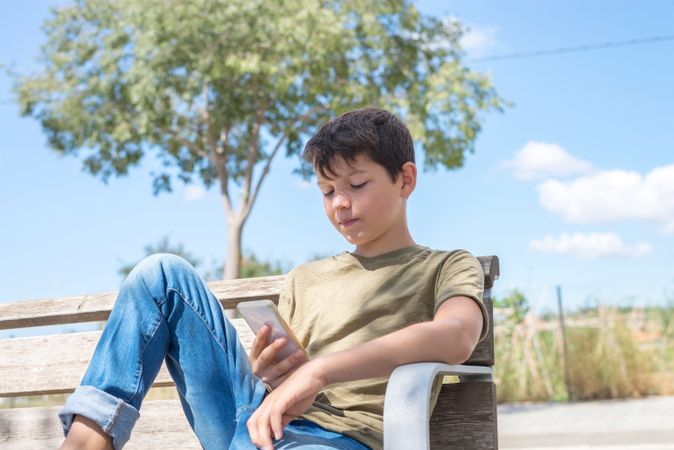 Boy sitting on bench looking at phone