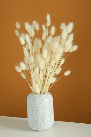 Vase of dried bunny tail bouquet centered on table in brown room, vertical composition