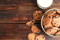 Tasty chocolate chip cookies and glass of milk on wooden table, top view. Space for text