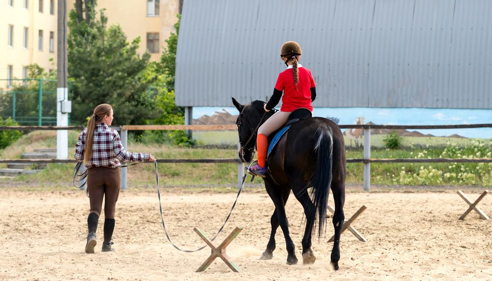 Instructor leading young rider during training session outdoors.