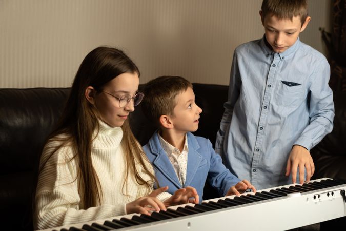 Three children gathered around keyboard, playing together.