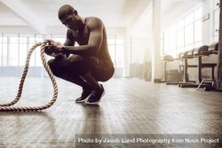 Man sitting on his toes holding a pair of battle ropes for workout 56KPY4