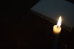 Top view of candle lit in the dark with copy space and notebook in background