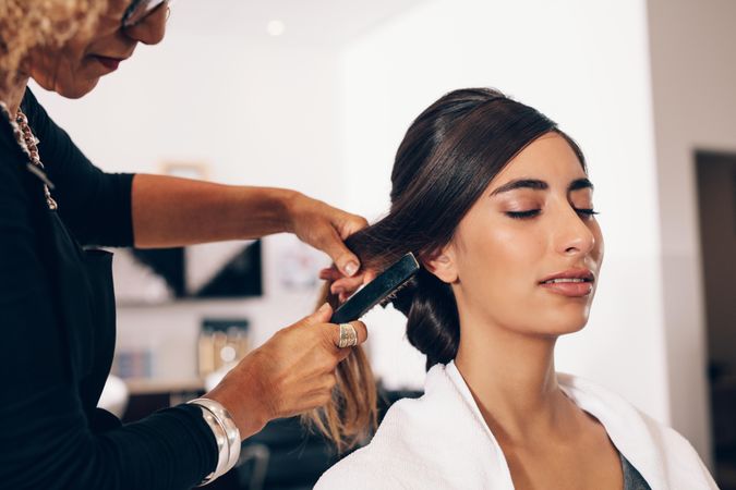 Relaxed young woman closing her eyes while hairdresser combs hair
