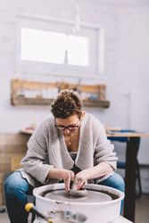 Woman potter shaping vessel on wheel