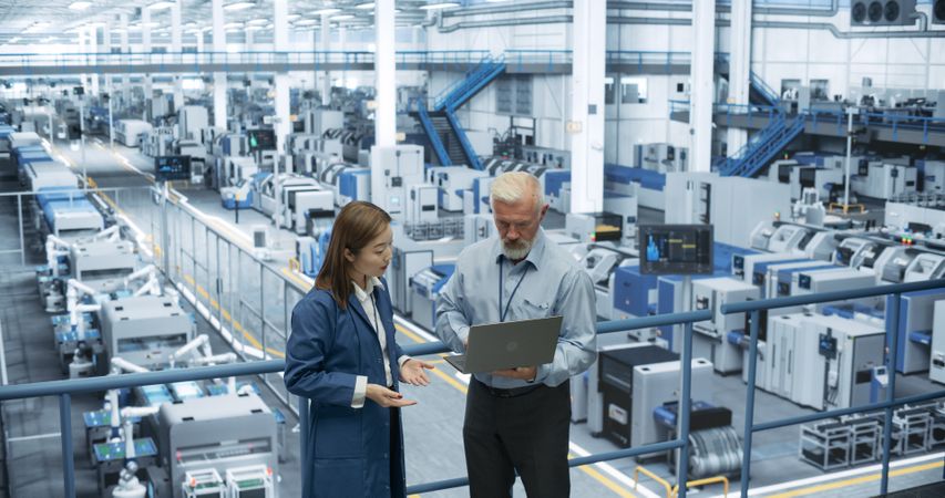 Industrial Engineers Working at a Technology Factory. White Man and Japanese Female Using Laptop Computer and Having a Conversation. Portrait of a Couple at Work