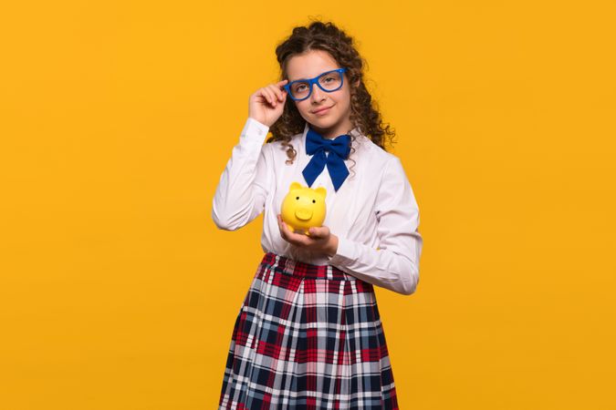 Girl adjusting blue glasses, holding piggy bank