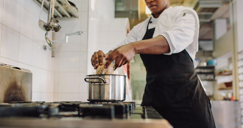 Chef adding food ingredients in stainless steel pot on stove